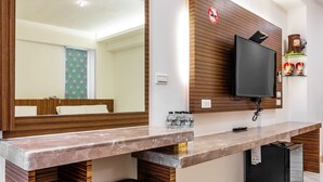 Un baño moderno con tocador de madera, un espejo grande, una televisión y un refrigerador pequeño.