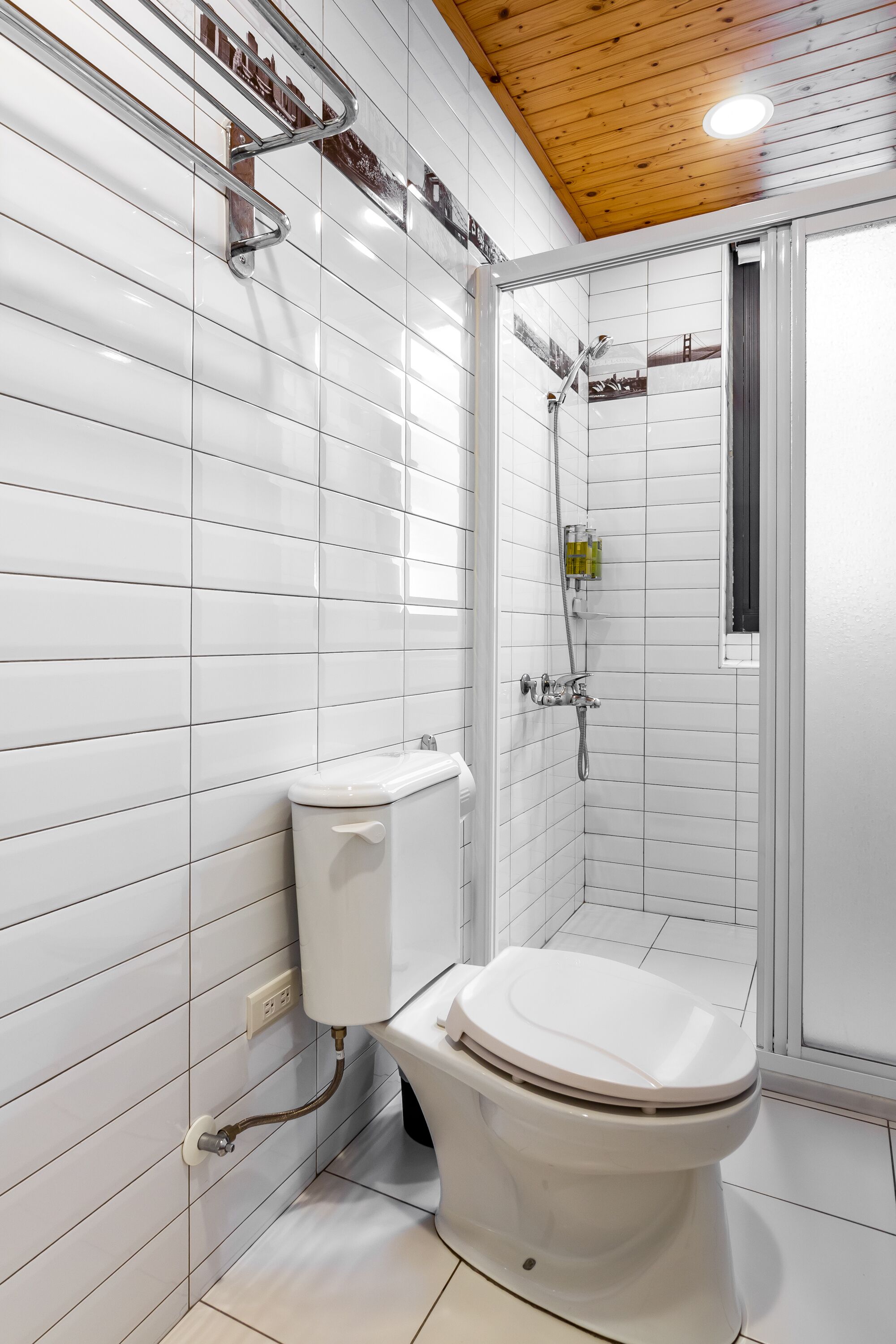 Ein Badezimmer mit weißen Fliesenwänden, einer Holzbalkendecke, einer Toilette und einer Duschkabine.