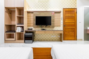 A hotel room with a wooden desk, a flat-screen TV, a wardrobe, and two beds.