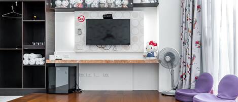 A modern hotel room with a flat-screen TV, a minibar, a small fridge, a fan, and a bed.