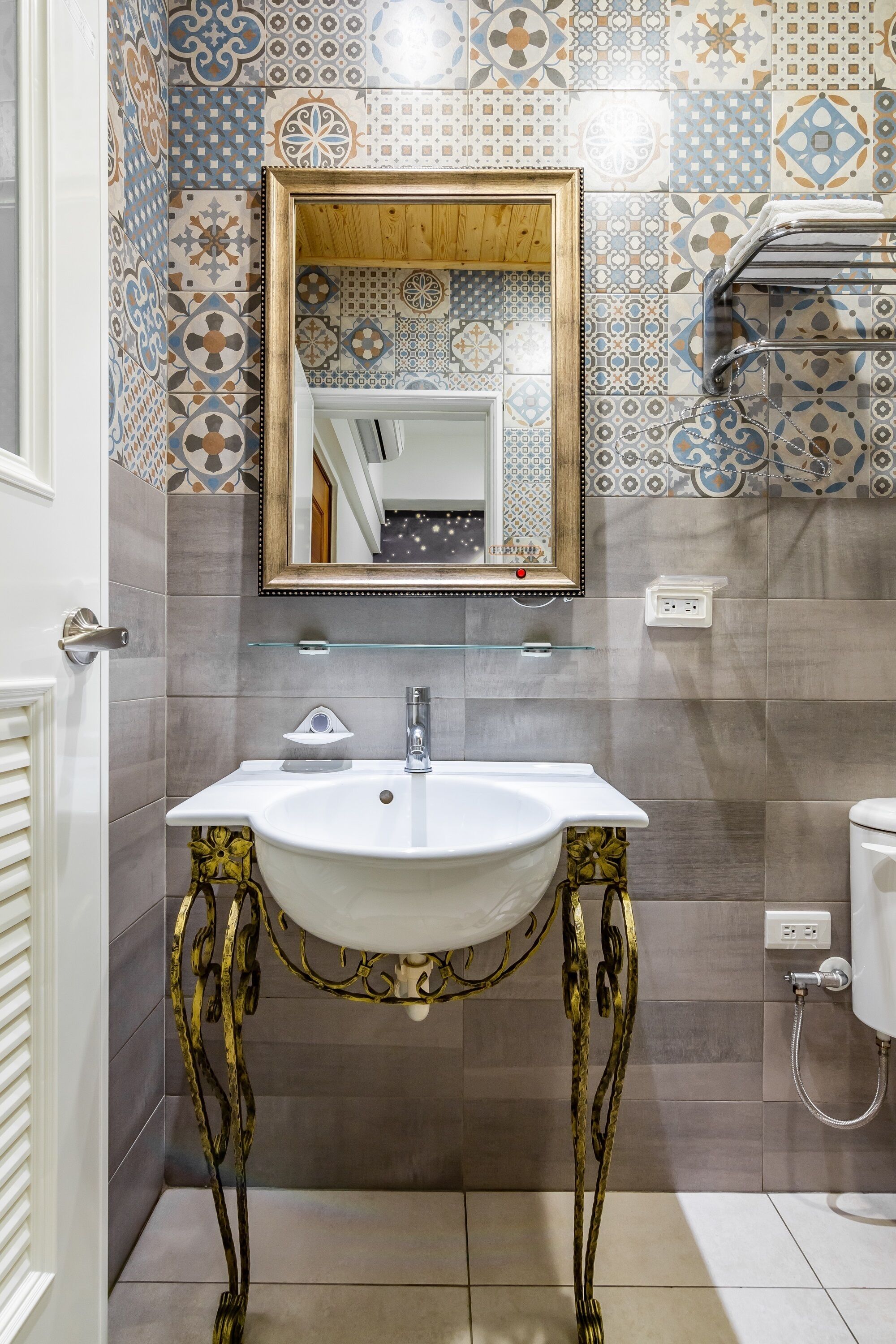 Un baño con lavamanos blanco, espejo y azulejos estampados.