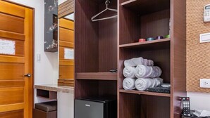 Habitación de hotel con un armario de madera, un refrigerador pequeño, un espejo y una estantería con toallas.