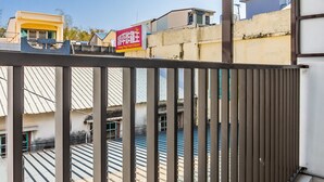 Un balcón con barandillas metálicas que da a una terraza con edificios al fondo.