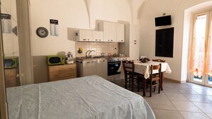 A compact kitchen with a microwave, oven, and sink. There's a dining table with chairs and a bed with a white bedspread. - Fittasi Studio in Ostuni (BR) (Ostuni)