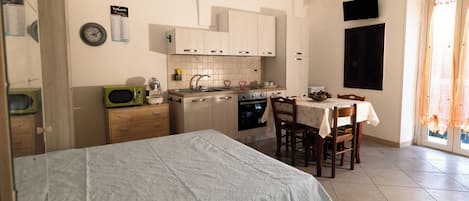 A compact kitchen with a microwave, oven, and sink. There's a dining table with chairs and a bed with a white bedspread.