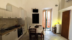 A compact kitchen with a dining area, a TV mounted on the wall, and a door leading to a bright room. - Fittasi Studio in Ostuni (BR) (Ostuni)