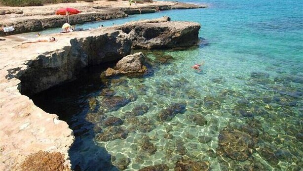 A rocky coastline with clear water, a red umbrella, and a person swimming. - Fittasi Studio in Ostuni (BR) (Ostuni)