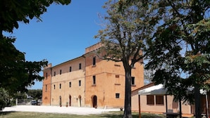Un grand bâtiment à plusieurs étages, doté d’un toit plat et de fenêtres en arc de cercle, entouré d’une zone herbeuse et d’arbres.