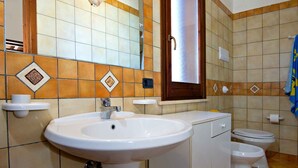 Un baño con un lavabo blanco, dos inodoros, un espejo y una ventana.