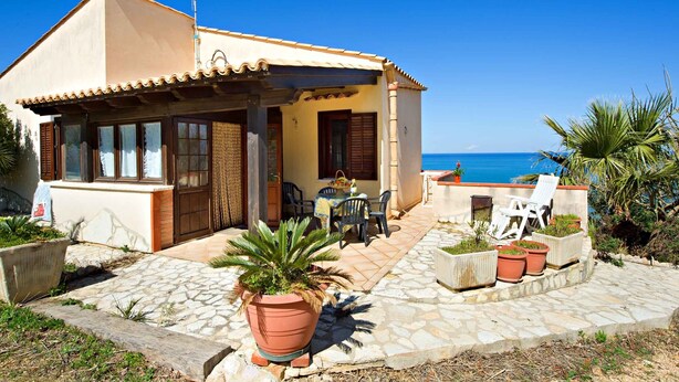 Una casa costera con patio de baldosas, mobiliario exterior y vista al mar.