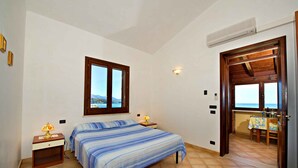 Un dormitorio con dos camas, una ventana con vista a la montaña, un equipo de aire acondicionado y una pequeña zona de comedor con una mesa y sillas.