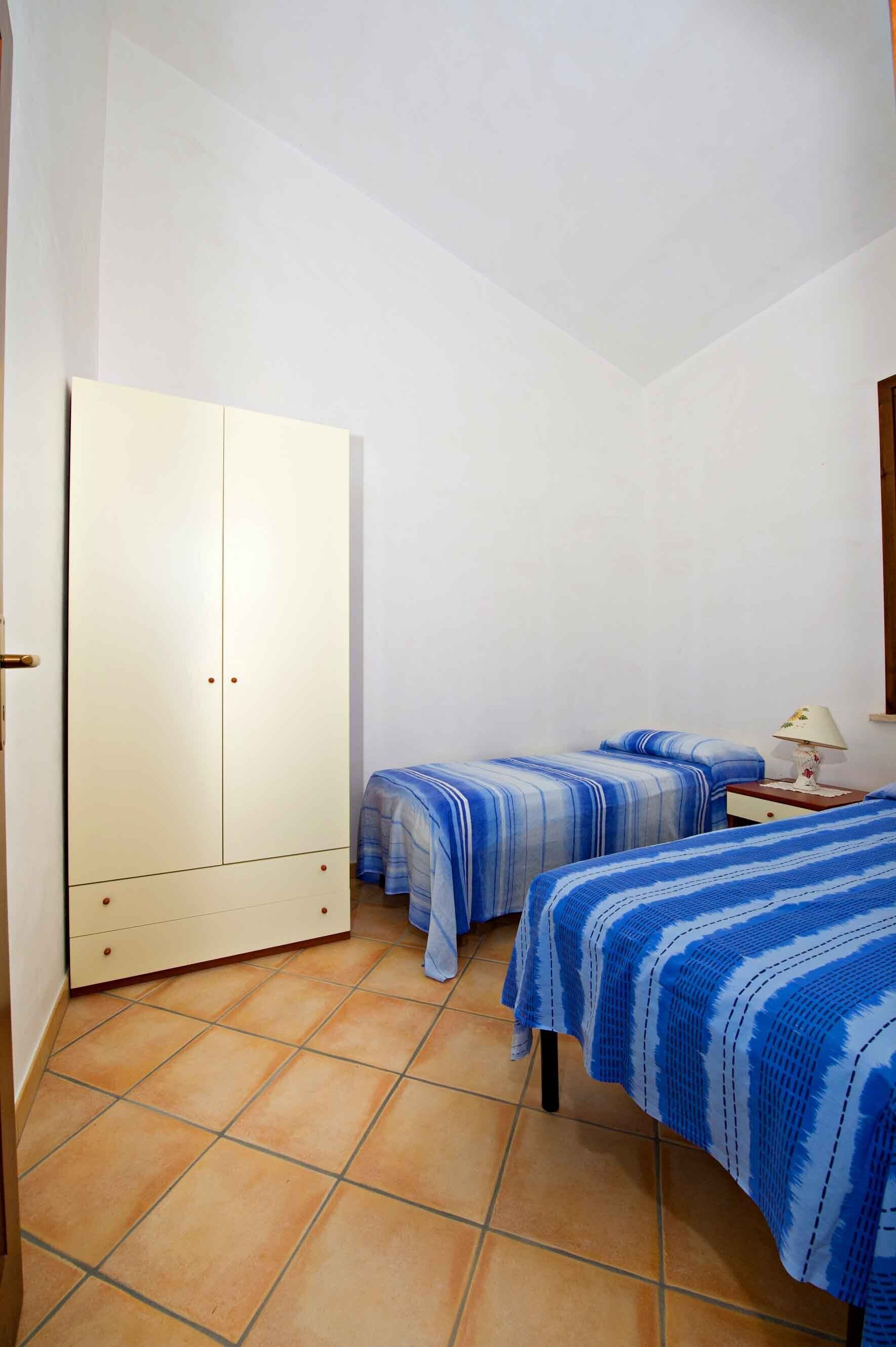Ein Zimmer mit zwei Betten, einem Schrank und einem Nachttisch mit Lampe.