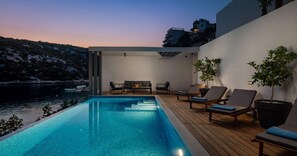 Un espace piscine extérieur moderne, doté d’une terrasse en bois, de chaises longues et d’un coin salon avec une table et des chaises.