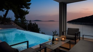 A modern outdoor seating area with a pool, overlooking a calm sea and distant land during twilight. - Beachfront Villa Eleganza with Pool (Marina)