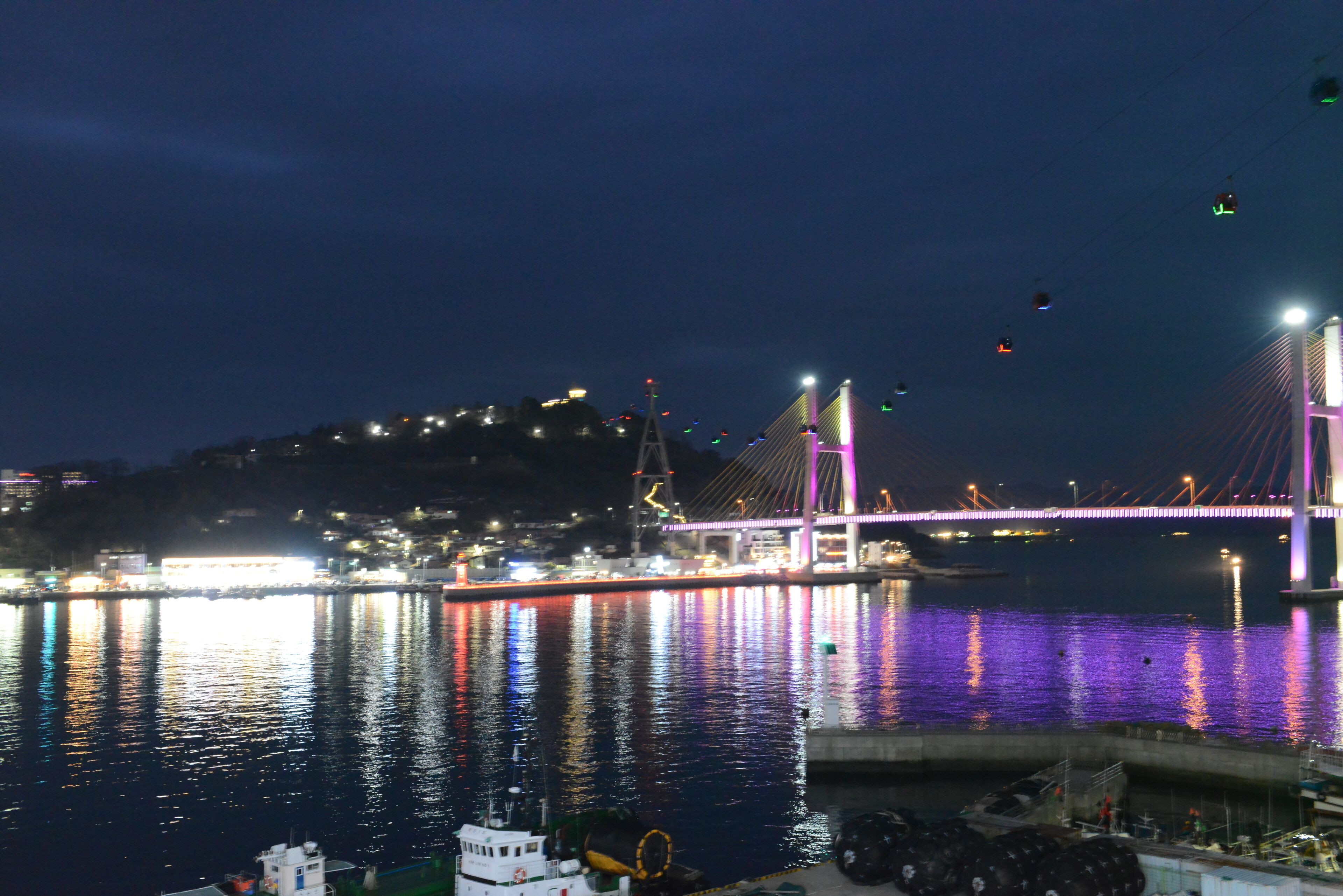 Vista noturna de uma ponte com luzes coloridas refletidas na água.