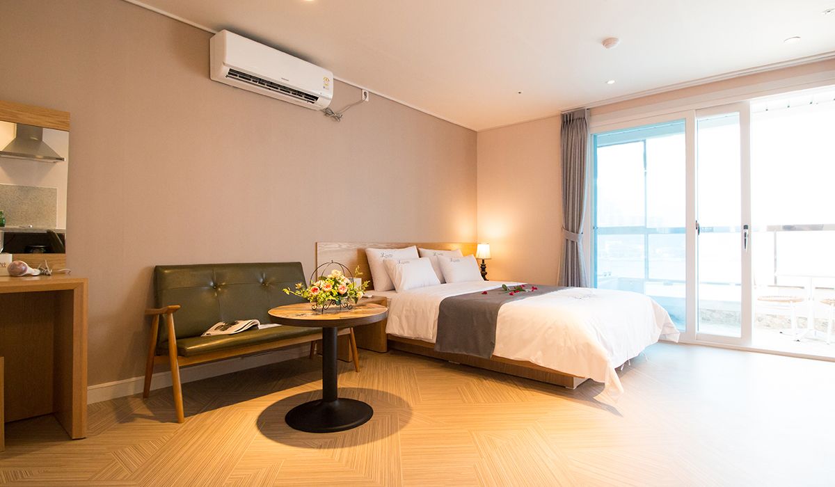 Habitació d'hotel amb un llit, un sofà, una taula rodona petita amb un ram de flors, un escriptori amb una làmpada i una finestra gran amb cortines.