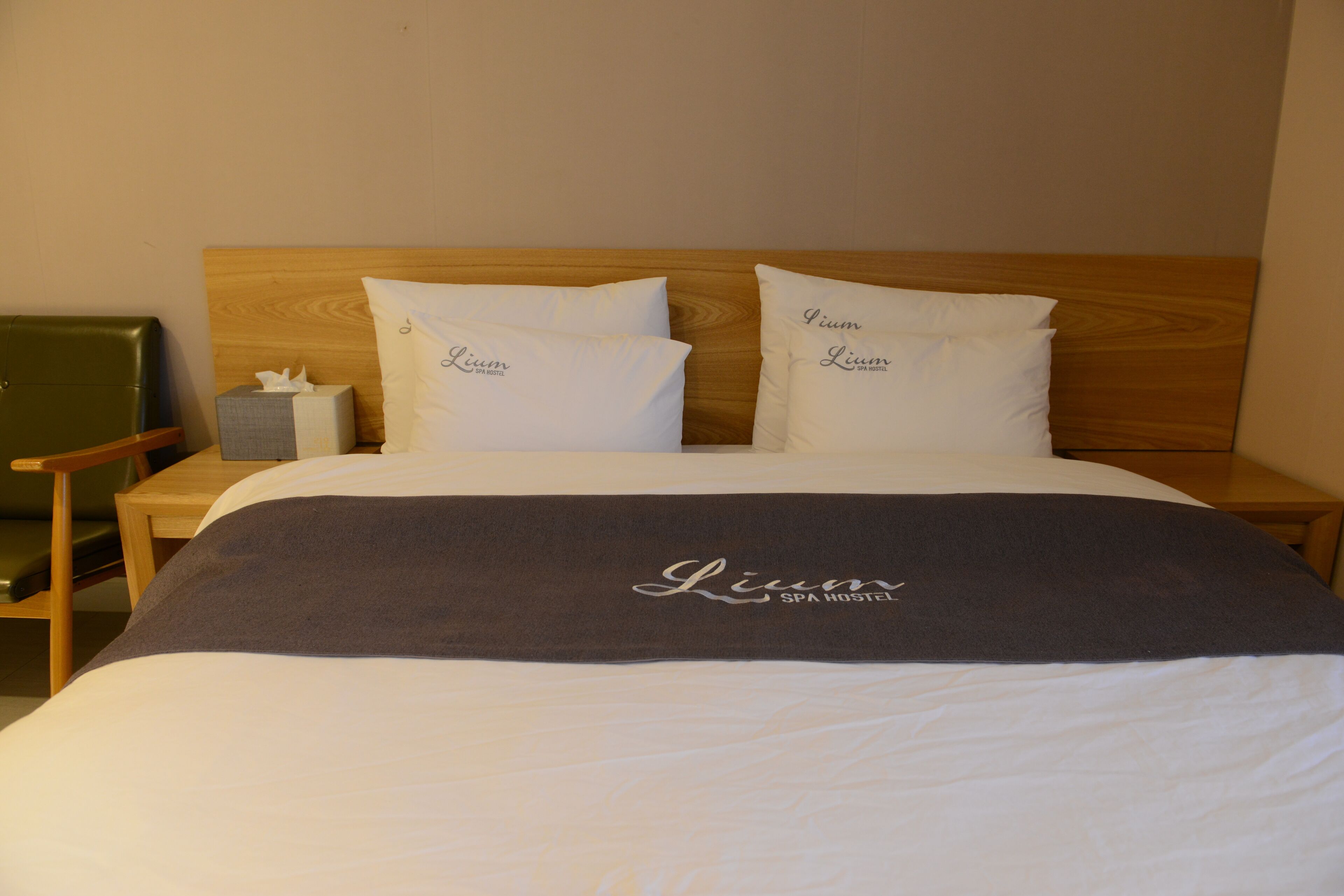 Un letto rifatto con due cuscini e una coperta, un comodino in legno con una scatola di fazzoletti e una sedia verde.