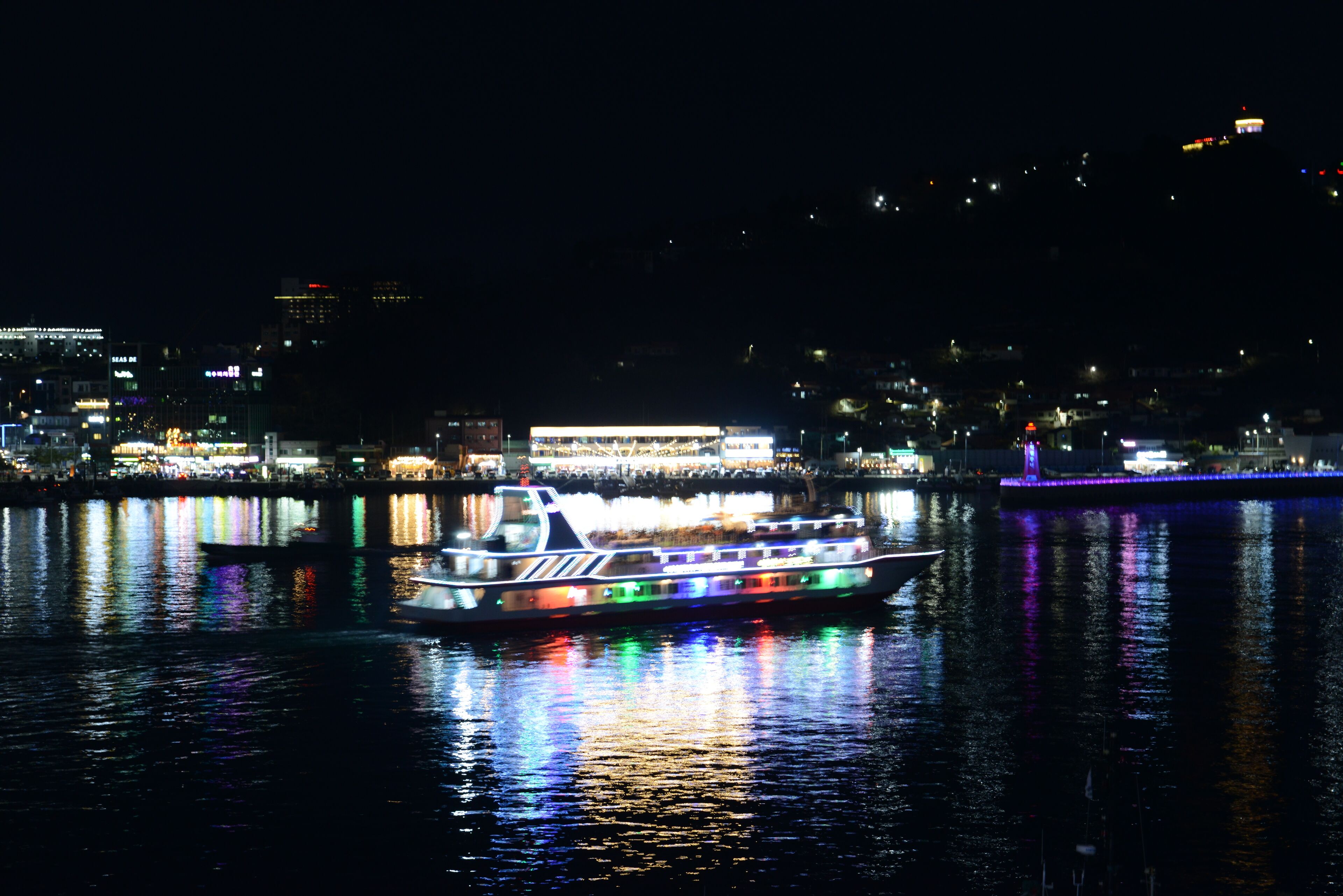 A boat with colorful lights on a river at night, reflecting on the water.