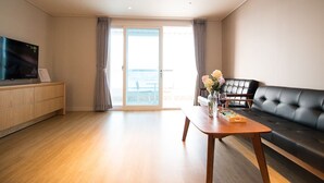 Una sala de estar moderna con piso de madera, un sofá de cuero negro, una mesa de centro de madera con un florero y un televisor de pantalla plana sobre un mueble de madera.
