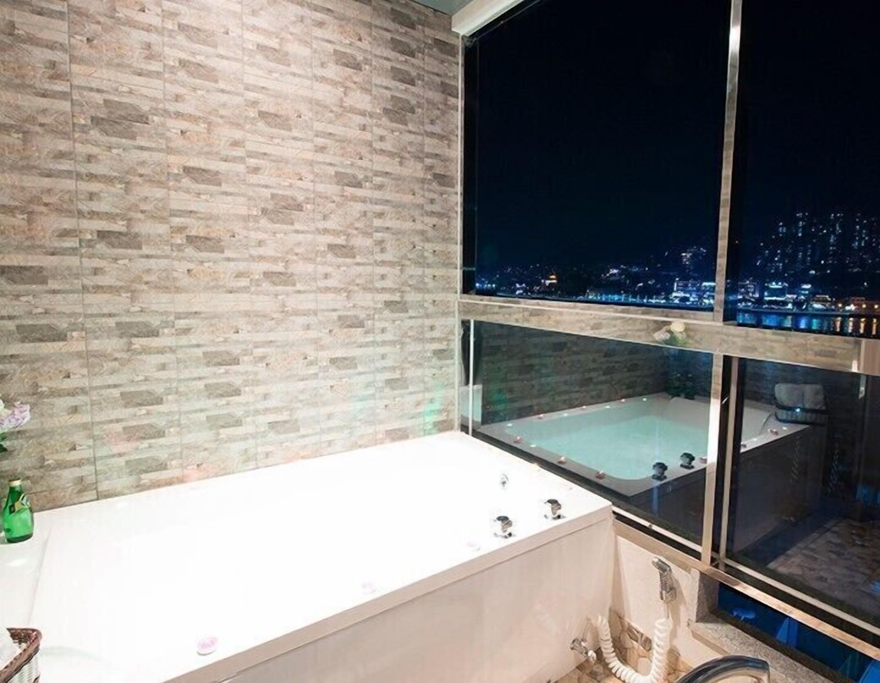 A modern bathroom with a large bathtub, a window with a city view, and a brick wall.