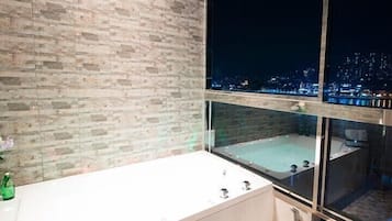A modern bathroom with a large bathtub, a window with a city view, and a brick wall.
