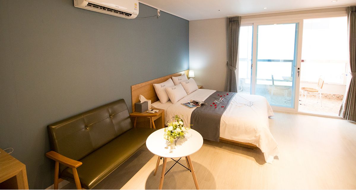 Camera d'hotel con un letto, un divano, un tavolino con un vaso e una porta-vetro scorrevole su un balcone.