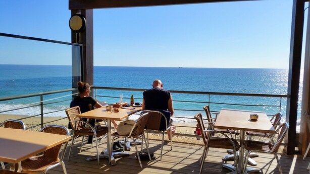 Une terrasse avec des tables et des chaises donnant sur la mer.
