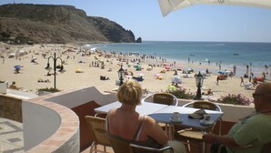 Un café situé en bord de mer, avec une terrasse offrant une vue sur une plage animée et l’océan.