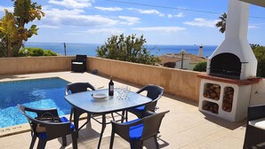 Une terrasse au bord de la piscine, avec une table et des chaises, un barbecue et une vue sur la mer.
