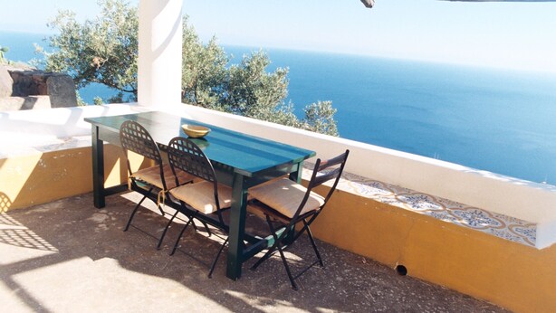A table and chairs on a balcony overlooking the sea.