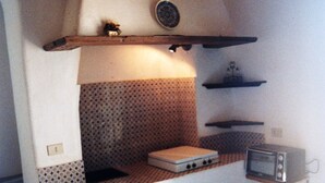 A compact kitchenette with a microwave, a small stove, and a shelf above the counter.