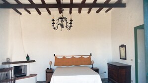 A bedroom with a checkered floor, a bed with a wooden headboard, a chandelier, a dresser, and a small table with a lamp.