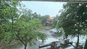 A wooden deck with a view of a river, dock, and house across the water.