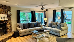 A living room with a stone fireplace, two sofas with patterned cushions, a coffee table, and a ceiling fan.