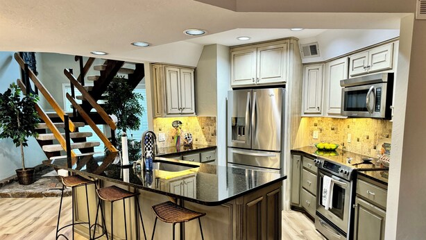 A modern kitchen with a central island, stainless steel appliances, and a staircase leading to another level.