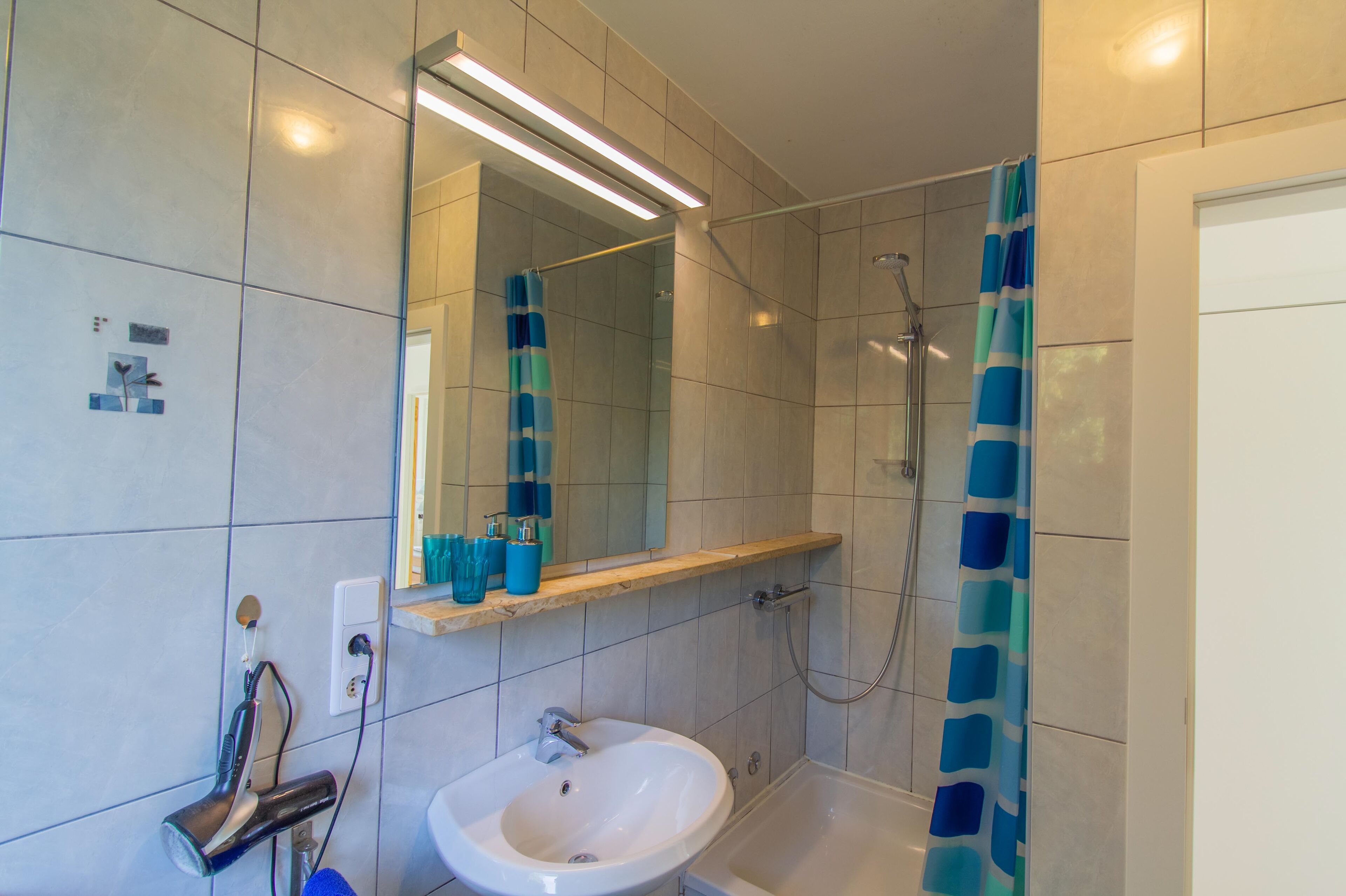 A bathroom with a white sink, a mirror, a shower, and a blue shower curtain.