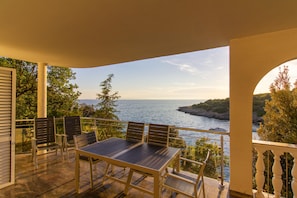 A balcony with a table and chairs overlooking a body of water and greenery.