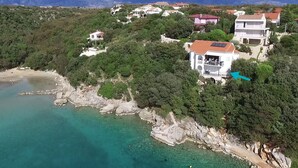 A coastal area with houses surrounded by greenery and a clear turquoise sea. - Beach Apartment 1: private bathing area, sandy beach, WiFi, ideal for families (Novalja)