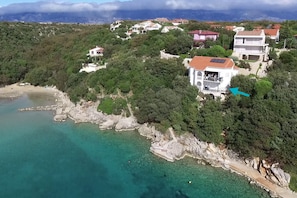 Eine Küstenlandschaft mit Häusern, umgeben von viel Grün, und einem klaren, türkisblauen Meer.