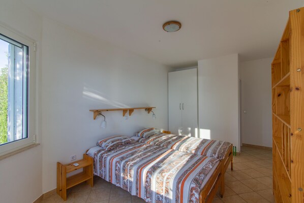 A bedroom with a bed, a wooden nightstand, a wardrobe, and a window.
