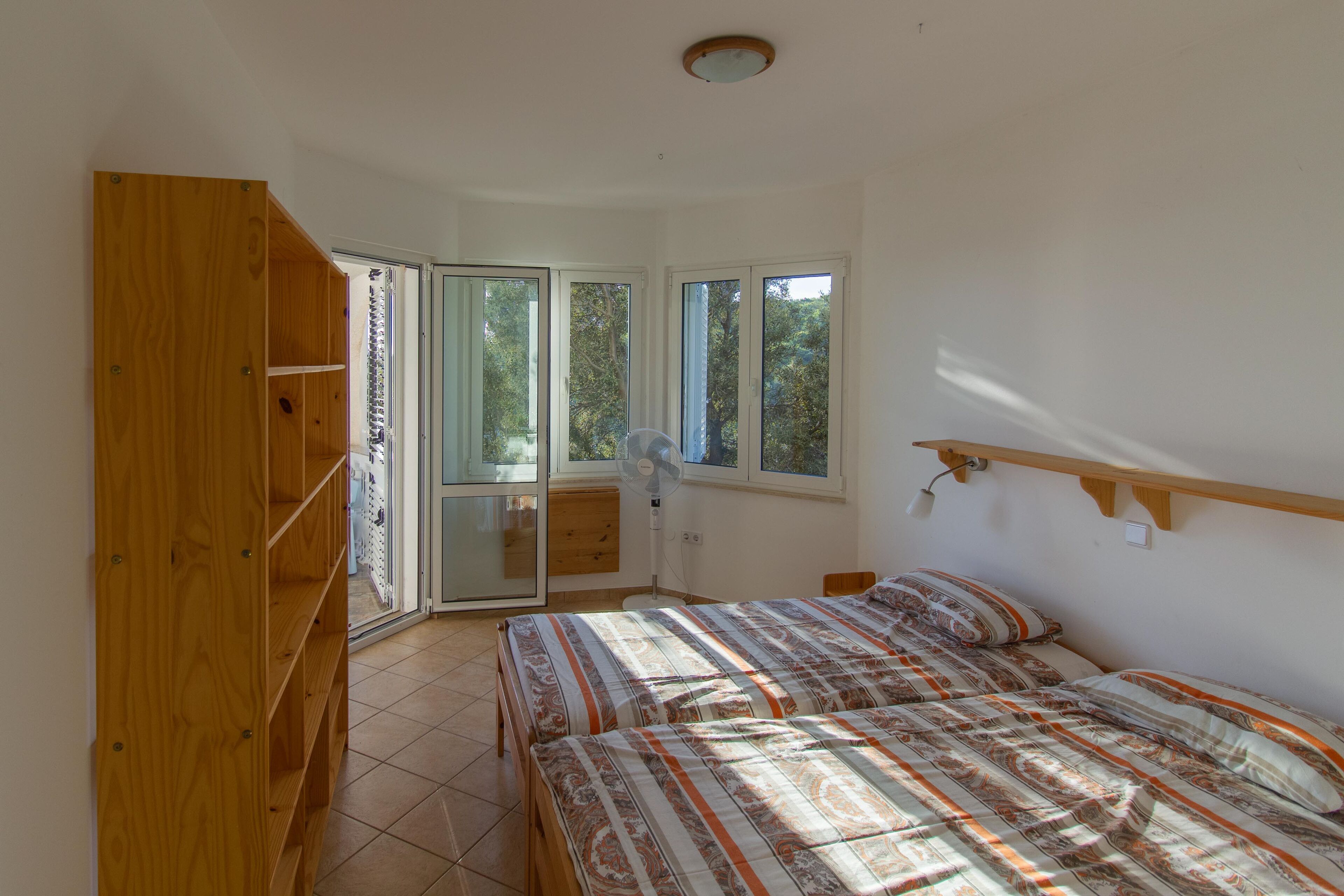 Un dormitorio con una cama, un armario de madera, una ventana y un ventilador.