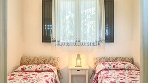 A room with two beds, each with floral bedding, a nightstand with a lantern, and a window with sheer curtains. - Cappero Pool House by Galatea Holiday Homes (Gagliano del Capo)