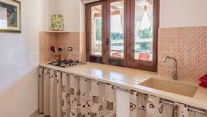 A kitchen with a gas stove, a sink, and a window with curtains. - Cappero Pool House by Galatea Holiday Homes (Gagliano del Capo)