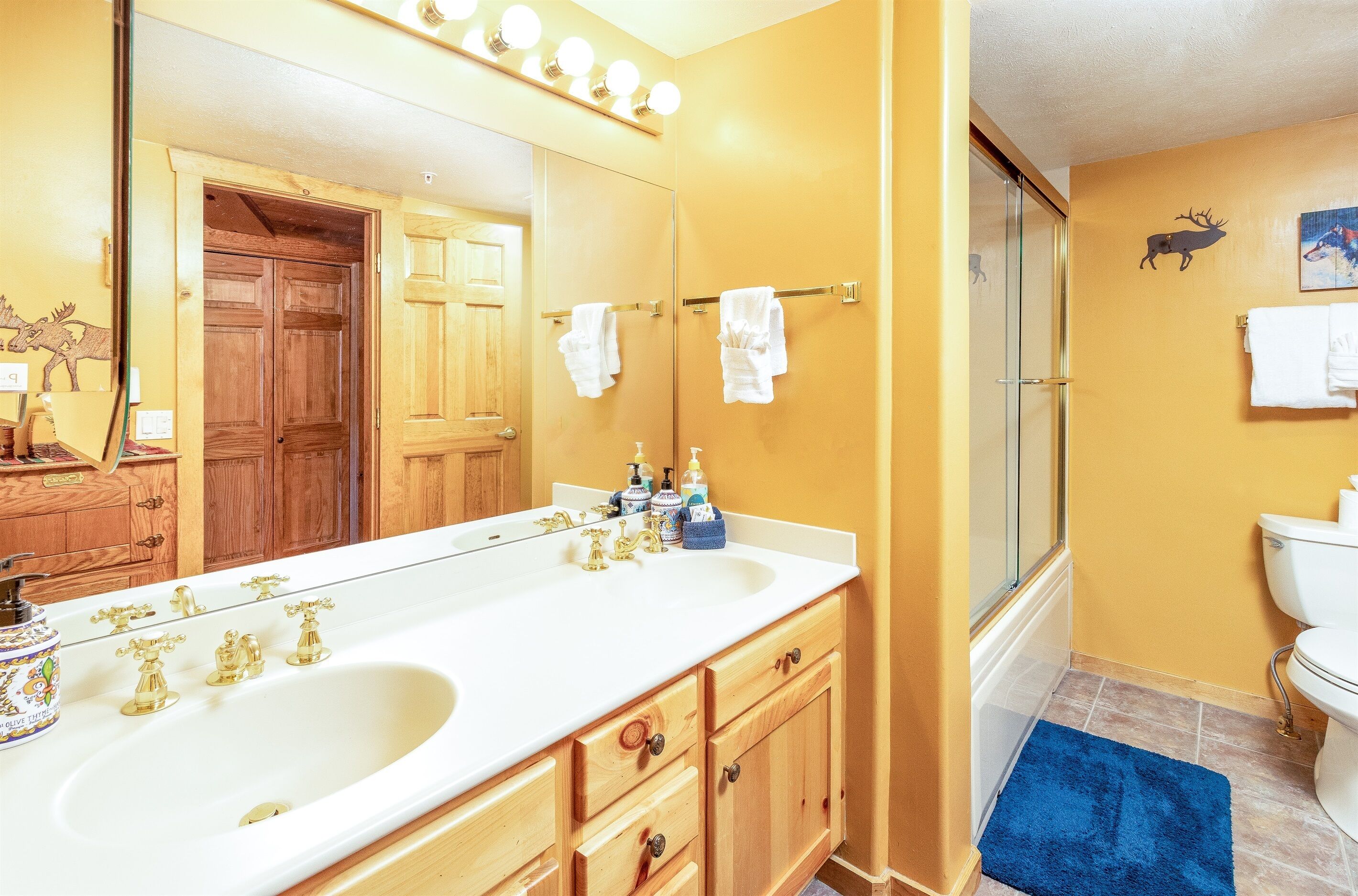 A bathroom with a double sink, wooden cabinets, a large mirror, and a shower area.