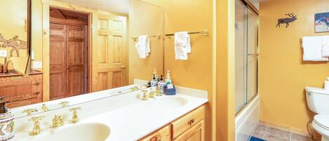 A bathroom with a double sink, wooden cabinets, a large mirror, and a shower area.