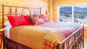 A wooden cabin bedroom with a large bed, a nightstand, a lamp, and a window with a mountain view. - Unique 7th Floor Penthouse. Views. Hot Tub Balcony (Frisco)