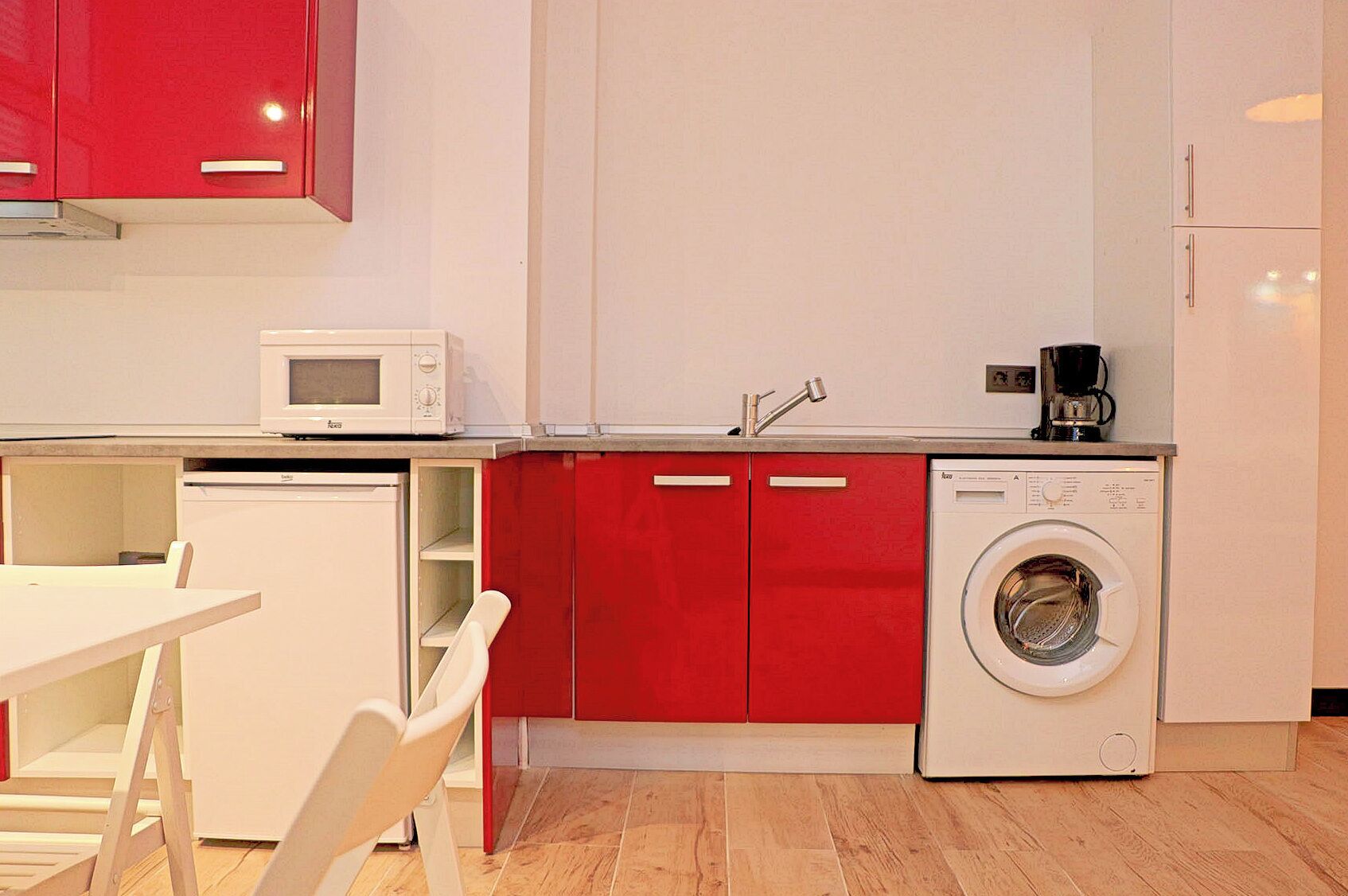A compact kitchen with a microwave, coffee maker, and washing machine.
