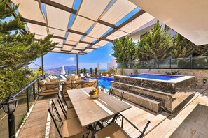 Ein Außenpoolbereich mit Tisch und Stühlen, einem kleinen Pool und Blick auf das Meer und die Berge.