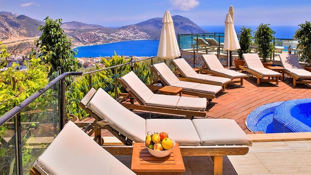 A rooftop terrace with lounge chairs and a pool, overlooking a coastal landscape.