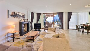 A modern living room with a sofa, a TV, a fireplace, and a dining area with a table and chairs.